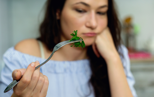 Woman in blue top looking at lettuce on fork with sad or discouraged face