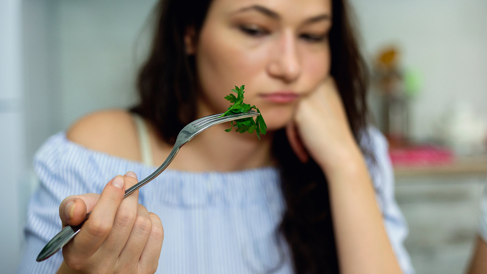 Woman in blue top looking at lettuce on fork with sad or discouraged face